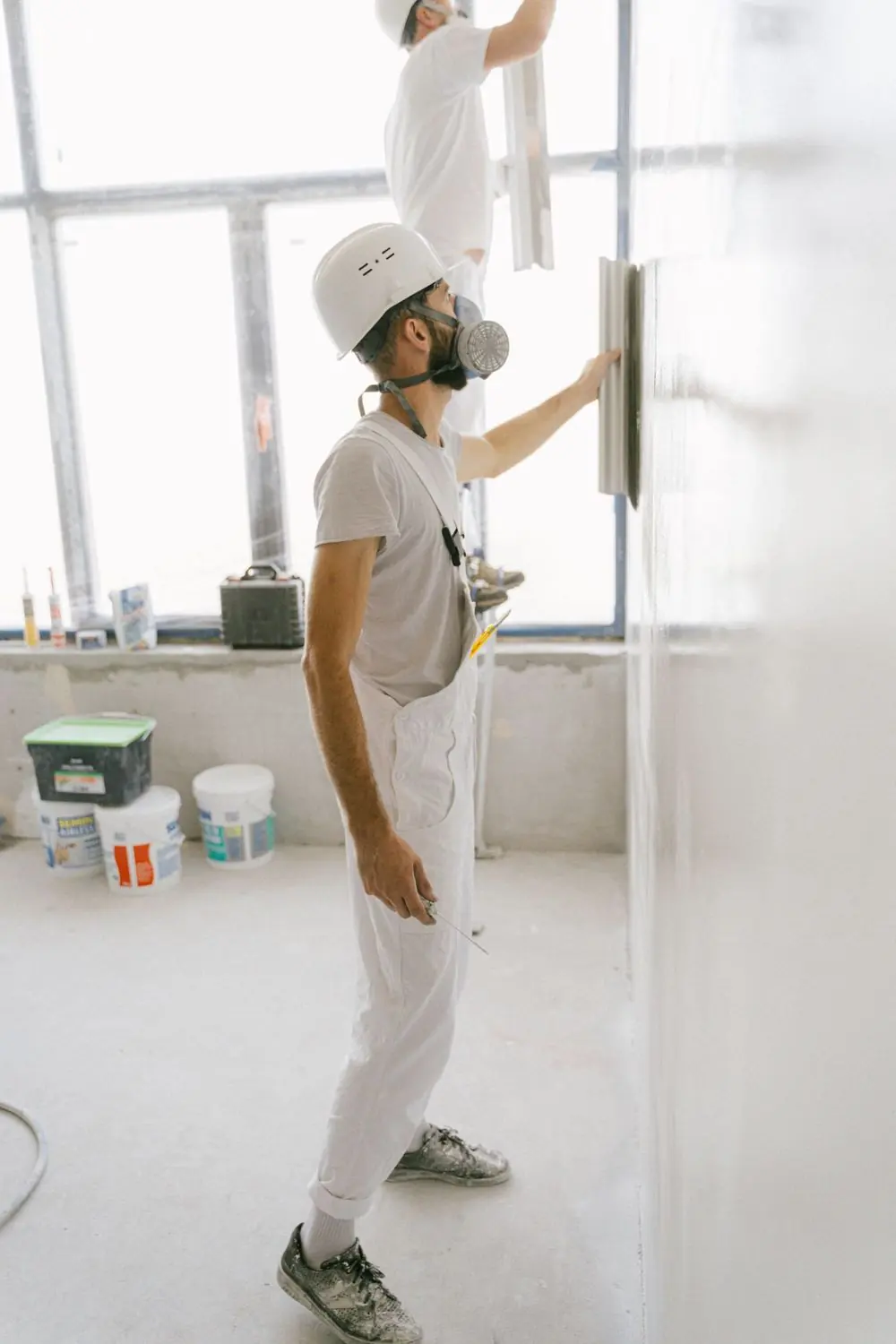 Schilder in witte overall werkt met stofmasker aan een wand
